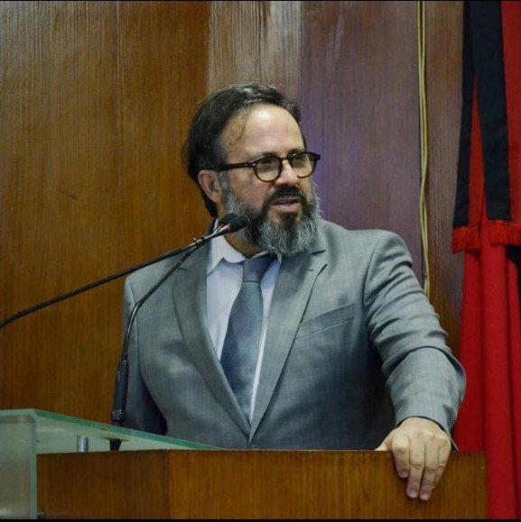 Dr. Fabio Firmino Araújo discursando em tribuna, trajando terno cinza